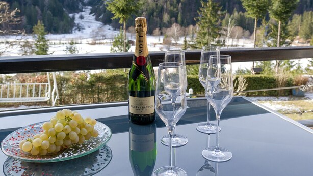 Une bouteille de champagne Moët & Chandon, deux verres et une assiette de raisins sur un balcon avec vue sur la montagne.