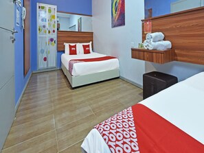 Habitación de hotel con cama, mesita de noche, espejo, cabecero de madera, repisa en la pared con toallas y puerta con teléfono y calendario.