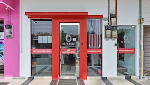 Entrada de hotel con un arco rojo y puertas de cristal, mostrando el nombre y el logotipo del hotel.