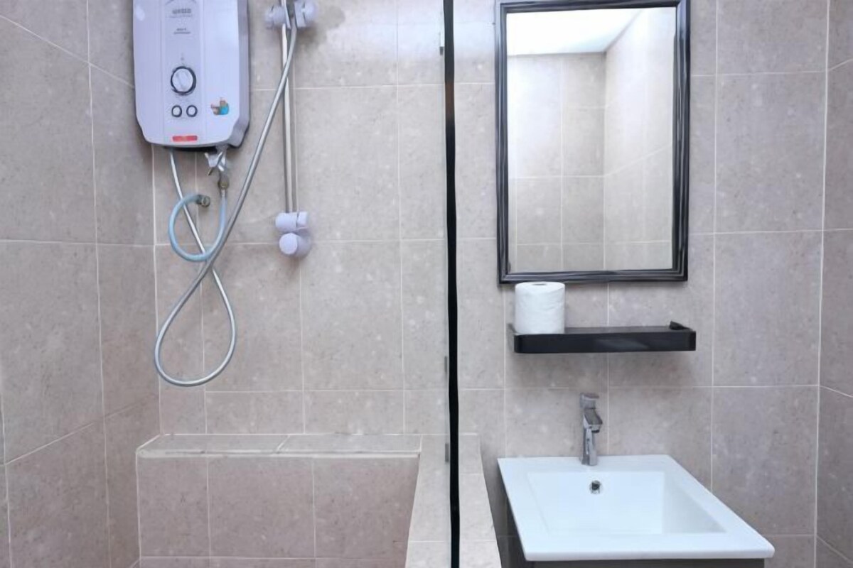 A bathroom with a shower, a sink, a mirror, and a towel dispenser.