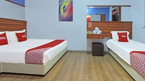 Habitación de hotel con dos camas, cada una con cubrecama y almohadas rojas y blancas, cabeceros de madera, mesitas de noche con artículos de tocador, y un cuadro abstracto de colores en la pared.