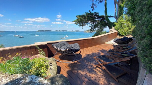 Un pontile di legno con una sedia a dondolo e poltrone relax che si affaccia su uno specchio d'acqua con barche.