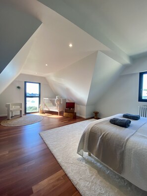 A high-ceilinged room with a sloped roof, a large bed with white bedding, a wooden floor, and a view through a large window. - "Heaven's door", exceptional villa feet in the water, direct access to the sea (Sarzeau)