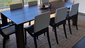 Un'area pranzo moderna con un tavolo grande e sedie, ampie finestre che offrono vista sul mare e sulle imbarcazioni, e un termosifone a parete.