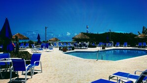 A poolside area with lounge chairs and umbrellas, a clear sky, and a calm pool.