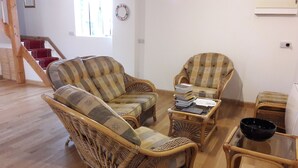 Un salon avec des meubles en osier, une table basse en verre et une bibliothèque.