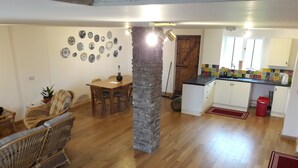 A spacious living area with a dining table, wicker furniture, a stone pillar, and a kitchen with white cabinets and a tiled backsplash.