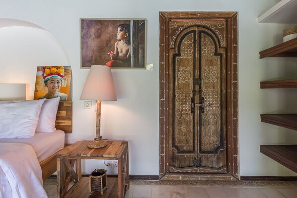 Un dormitorio con cama, una mesita de noche con lámpara, una puerta decorativa y un cuadro en la pared.