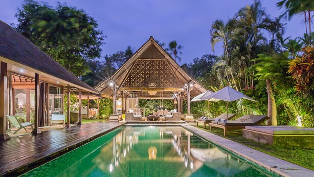 Uma área à beira da piscina com um espaço de estar coberto, espreguiçadeiras e piscina.