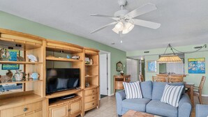 Un salon équipé d’un téléviseur, d’un meuble de rangement en bois, d’un canapé bleu et d’un ventilateur de plafond.