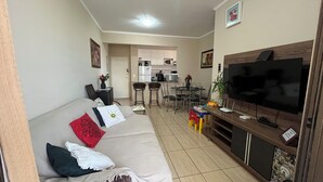 Un salón con sofá, televisión y cocina al fondo.