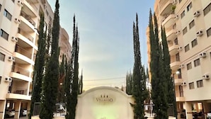 Entrada de hotel moderna con un letrero destacado, altos árboles y cielo despejado.