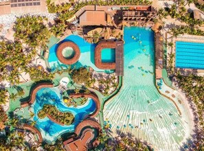 An aerial view of a resort with multiple swimming pools, palm trees, and a beach area.