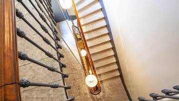 Una scala a chiocciola con ringhiere in metallo decorate e un corrimano in legno, che conduce a un pianerottolo con un lampadario.