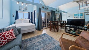 Ein Zimmer mit einem Bett, einer Couch, einem Fernseher, einem Esstisch und einer Treppe.