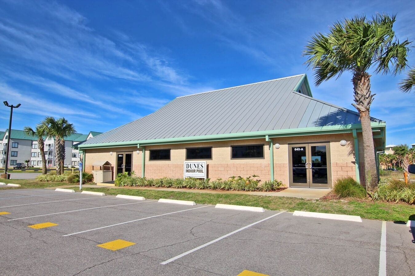 A building with a sign for an indoor pool, parking lot, and palm trees.