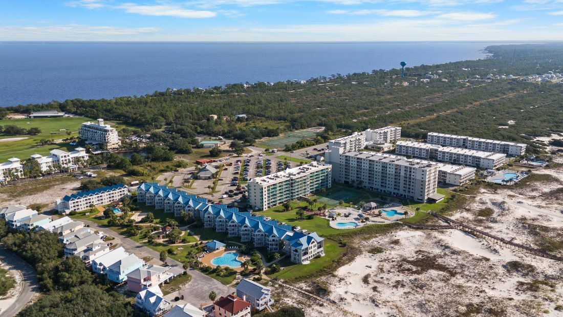 An aerial view of a coastal resort with multiple hotel buildings, a beach, and a clear view of the ocean.