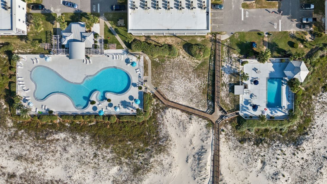 Ett flygbildsbild av ett semesterområde med två pooler, ett strandområde och en parkeringsplats.