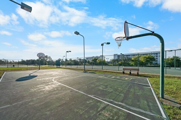 An outdoor basketball court with a bench and a basketball hoop.