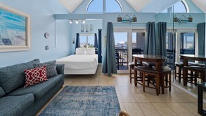Ein Schlafzimmer mit Bett, einer Couch, einem Esstisch mit Stühlen und einem Balkon mit Vorhängen.
