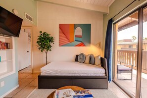 Un dormitorio con cama, televisor, estantería, planta y un cuadro.