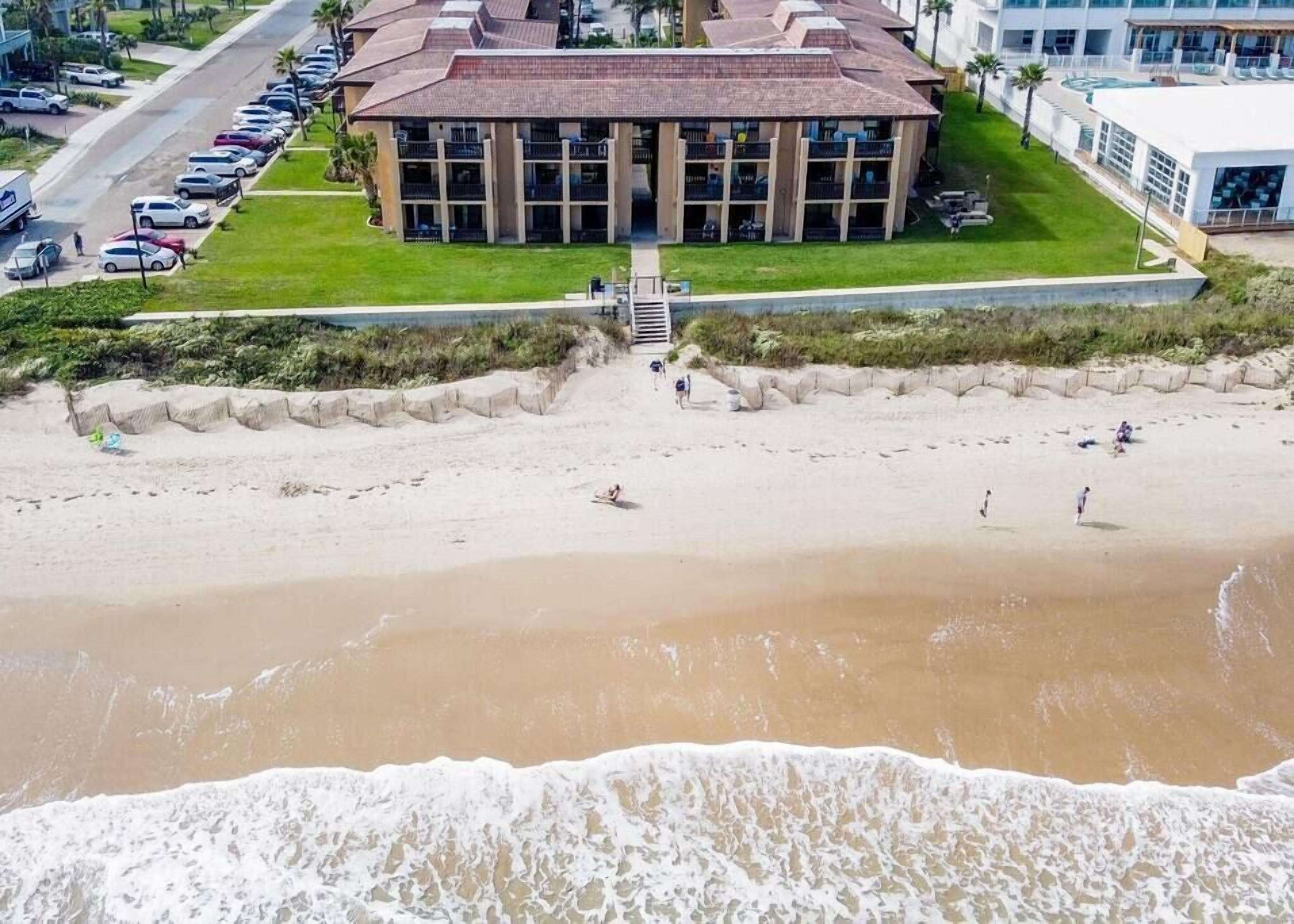 Un hôtel situé en bord de mer, doté d’un grand bâtiment, d’un parking et d’une plage de sable.