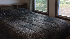 A bedroom with a large bed, a painting on the wall, and a window with a view of trees. - Rivers Edge/Off Grid/ Bird Watching Summer Paradise (Paradise)