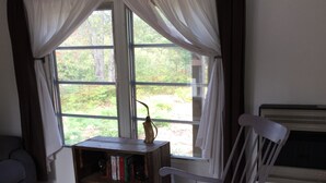 A room with a rocking chair, a small wooden table with a vase, and a bookshelf. - Rivers Edge/Off Grid/ Bird Watching Summer Paradise (Paradise)