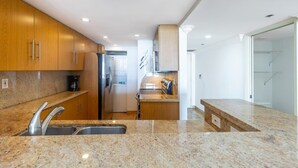 Une cuisine moderne dotée de plans de travail en granit, d’appareils électroménagers en acier inoxydable et d’armoires en bois.