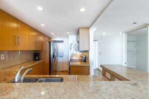 A modern kitchen with granite countertops, stainless steel appliances, and wooden cabinets. - Modern Long Stay Apt | Bayview Balcony | StayCozy (Miami)