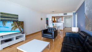 Un salon moderne avec un téléviseur à écran plat, un canapé en cuir noir, une table basse blanche et, au fond, un coin repas.