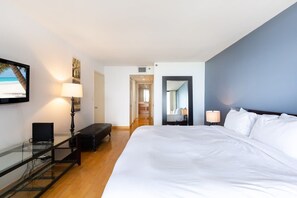 A hotel room with a large bed, a desk with a laptop, a lamp, and a TV on the wall. - Modern Long Stay Apt | Bayview Balcony | StayCozy (Miami)