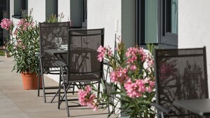 An outdoor seating area with metal chairs and tables, potted plants, and a building with large windows. - Apartment Unterlechnung in Vomp (Vomp)