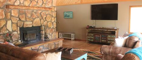 A cozy living room with a stone fireplace, leather sofas, a flat-screen TV, and a wooden ceiling.