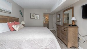 Een slaapkamer met een groot bed, een houten dressoir, een spiegel en lijstwerken aan de muren.