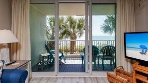Een balkon met uitzicht op palmbomen en de oceaan, voorzien van stoelen en een tafel.