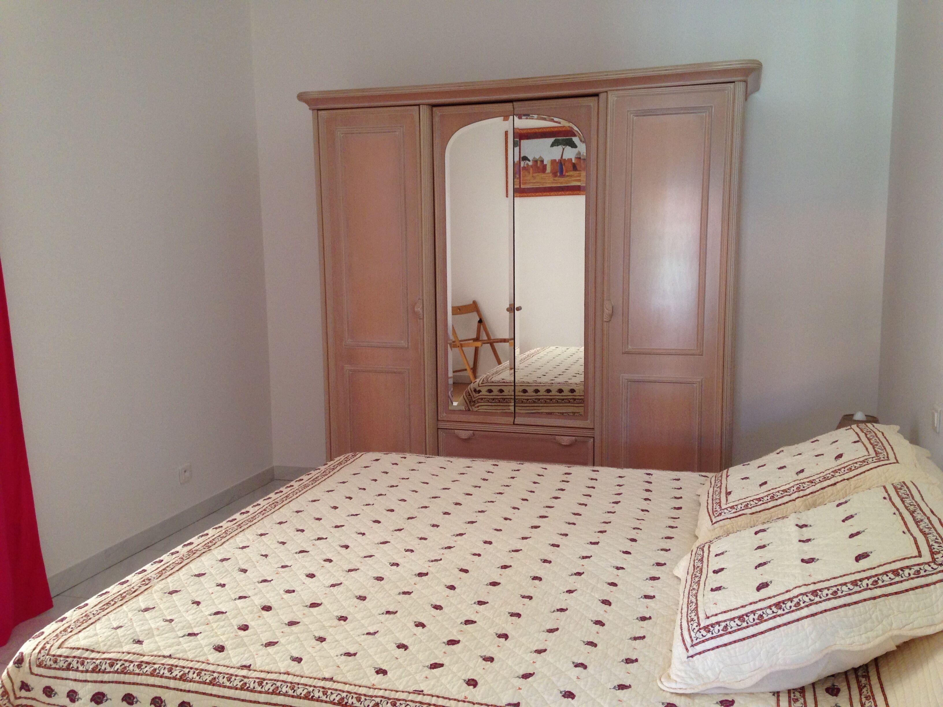 A bedroom with a bed, a wooden wardrobe, and a mirror.