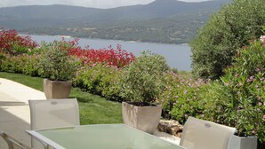 An outdoor seating area with a table and chairs, surrounded by potted plants and flowers, overlooking a lake and mountains.