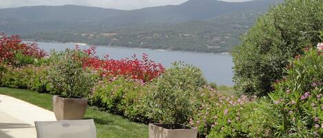 An outdoor seating area with a table and chairs, surrounded by potted plants and flowers, overlooking a lake and mountains.