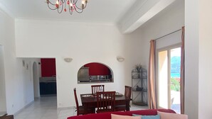 A spacious living area with a red sofa, a dining table with chairs, and a kitchen in the background.