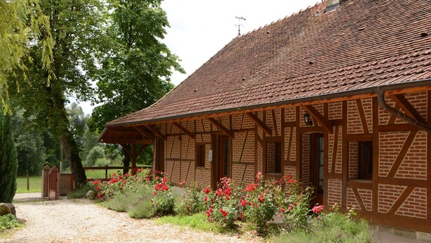 A traditional half-timbered building with a sloped roof, surrounded by a gravel path and flowering shrubs. - Beautiful bressane house 4/5 people (Le Tartre)