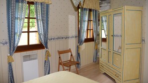 A room with a bed, a wooden chair, a wardrobe, and two windows with curtains. - Beautiful bressane house 4/5 people (Le Tartre)