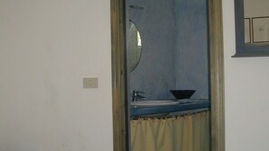Ein Schlafzimmer mit Bett, ein Badezimmer mit Waschbecken und Spiegel, und eine Tür zu einem anderen Raum.