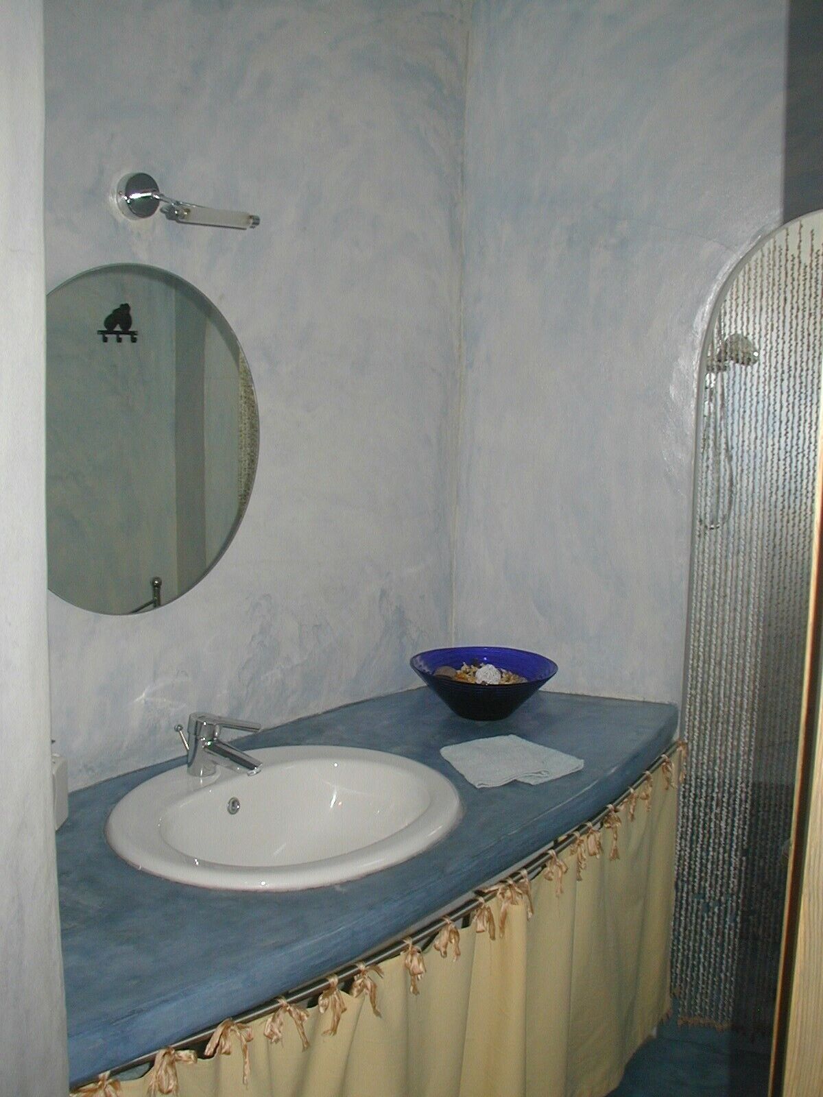 A bathroom with a white sink, a blue countertop, a mirror, and a blue bowl.
