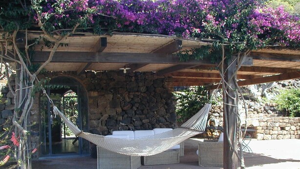 Eine Hängematte unter einer Holz-Pergola mit einer Steinwand im Hintergrund.
