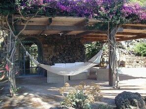 A hammock under a wooden pergola with a stone wall backdrop. - Ancient Dammuso with beautiful garden CIN: IT081014C2QNZ3XVTN (Pantelleria)