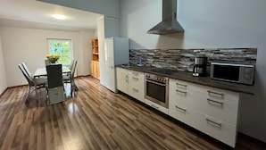 Une cuisine moderne avec un plancher en bois, des armoires blanches, une hotte de cuisinière en acier inoxydable, un four à micro-ondes et une machine à café.