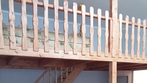 Une pièce avec un lit en mezzanine, un escalier en bois, un canapé noir et une petite table.
