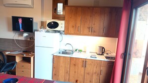 Ett kompakt kök med träskåp, en mikrovågsugn, ett handfat och en liten matplats med ett bord och stolar.
