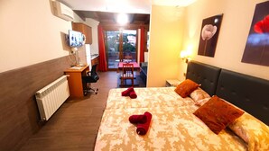 Ett hotellrum med en säng, ett skrivbord med en stol, ett element, en tv och ett fönster med gardiner.
